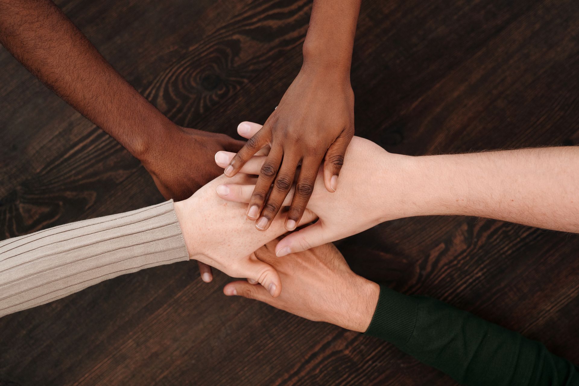 People joining hands together over a table, different skin tones side by side